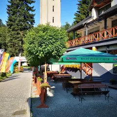 Taras restauracyjny z ławkami i stołami, parasolami, obok łuki startowe i flagi.