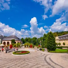 Urokliwy plac w Kudowie Zdrój z zabytkowymi budynkami, zielenią i kwitnącymi rabatami. Idealne miejsce na spacer pośród atrakcji.